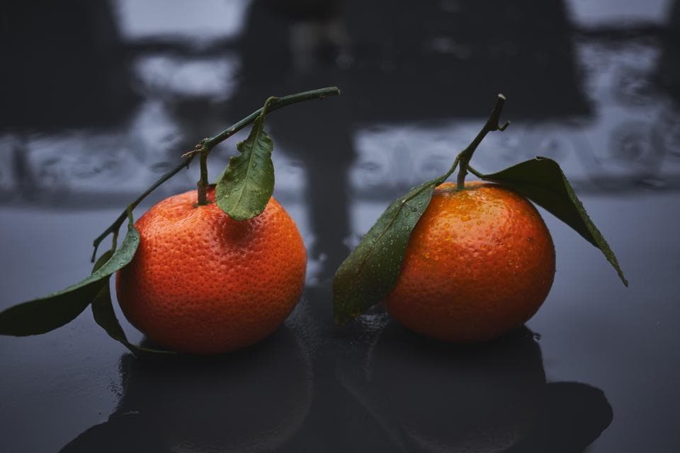 Două mandarine cu frunze verzi, pe o suprafață umedă și întunecată